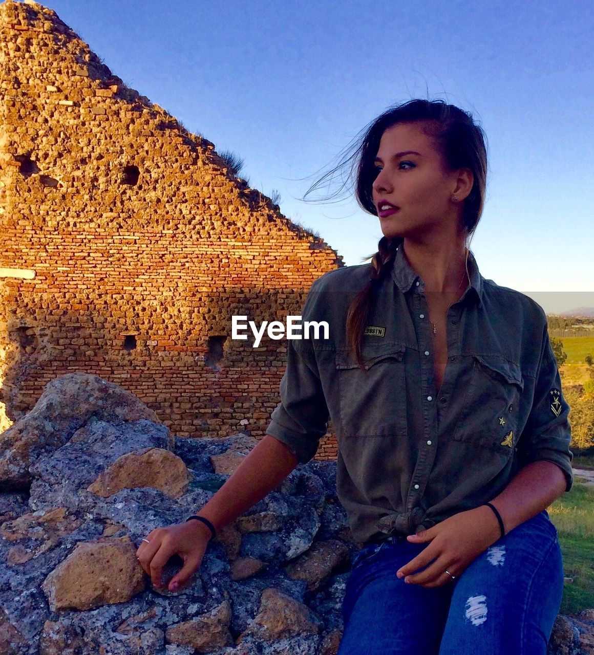 Young woman sitting on rock against old ruins