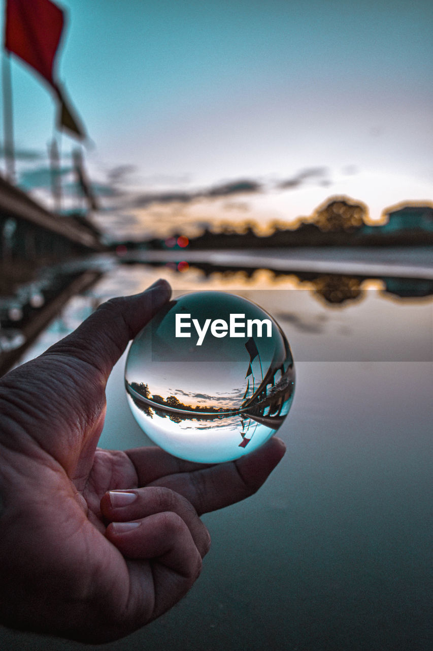 Close-up of hand holding crystal ball against sky during sunset