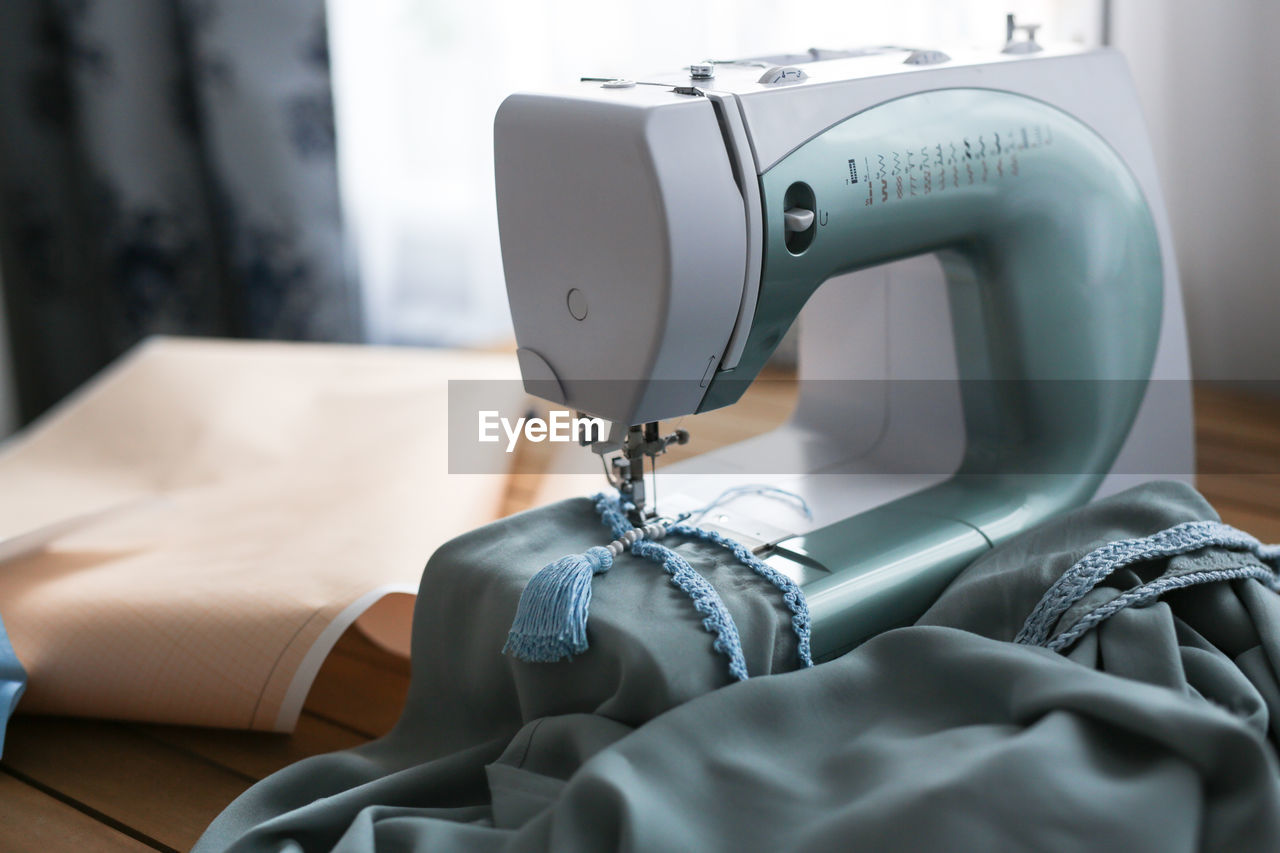 Background, sewing machine and fabric with patterns on wooden work table, opposite window 