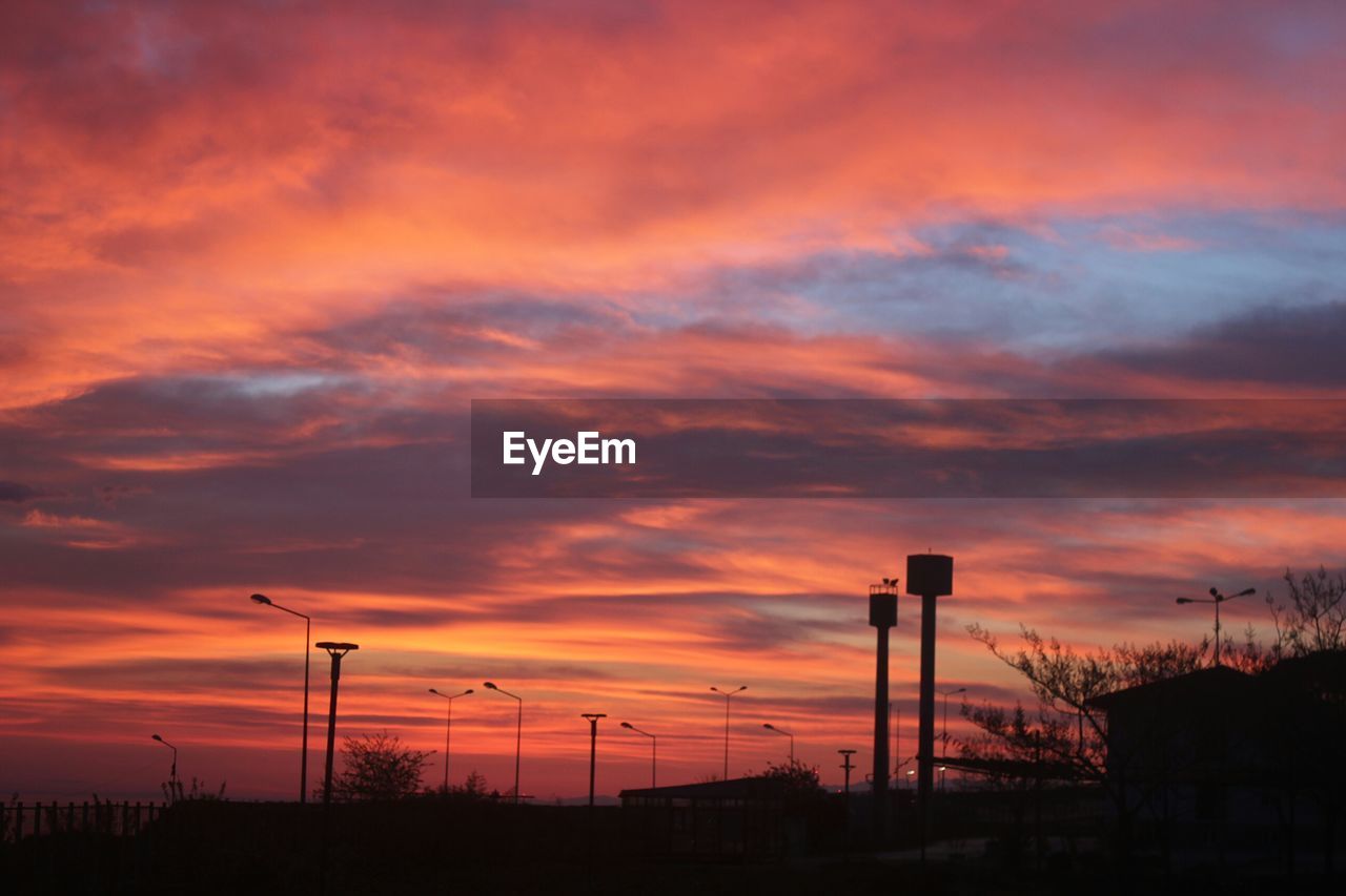 Silhouette street lights against dramatic sky during sunset