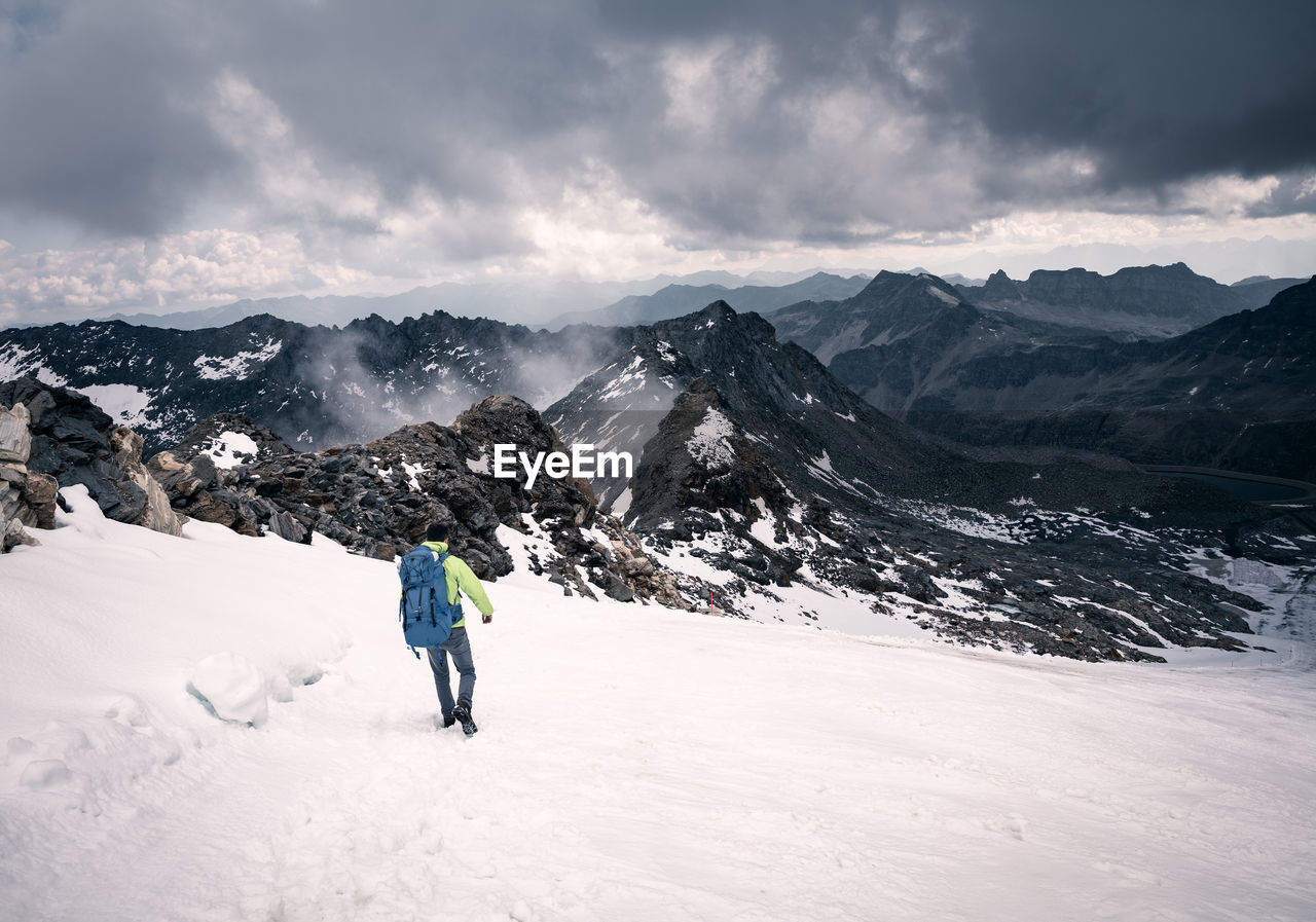 Rear view of backpacker on snowcapped mountains against cloudy sky