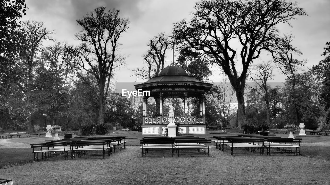 tree, plant, park, bench, black and white, park - man made space, nature, sky, monochrome, architecture, monochrome photography, seat, built structure, park bench, cloud, outdoors, day, travel destinations, water, building exterior, no people, gazebo