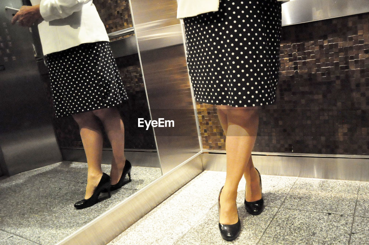 Low section of business woman using smart phone in elevator
