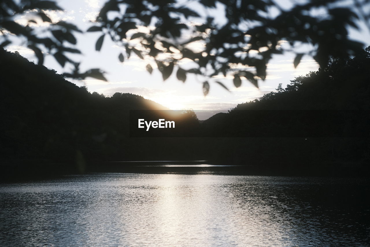 SCENIC VIEW OF LAKE BY SILHOUETTE TREES AGAINST SKY AT SUNSET