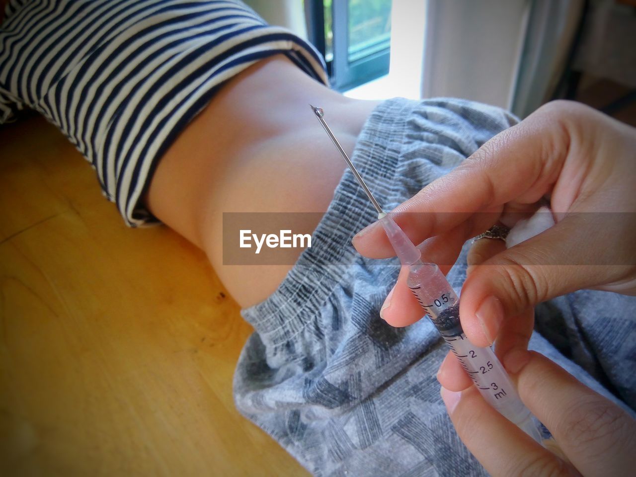 Cropped hands of doctor holding syringe while patient lying in background