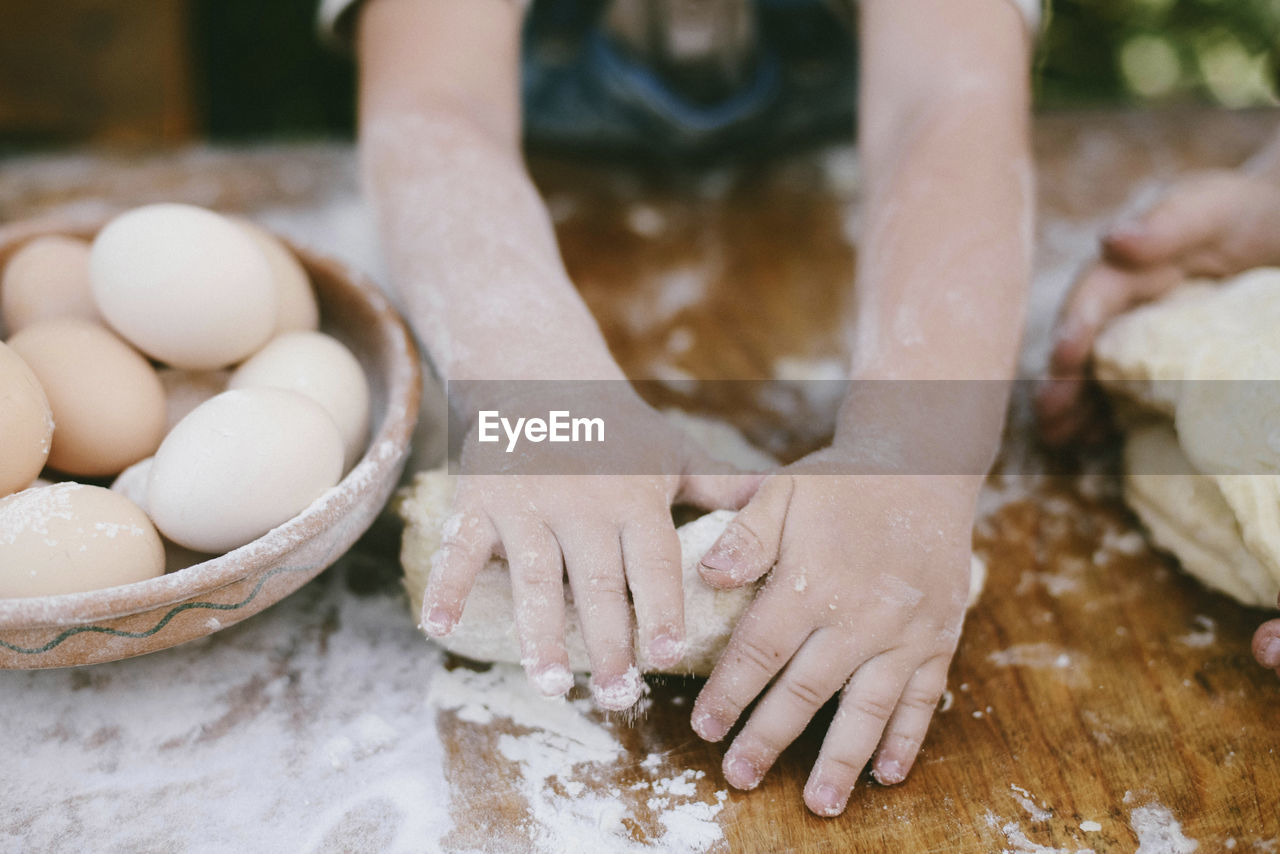 Cropped hands of mother and son kneading dough on wooden table at yard