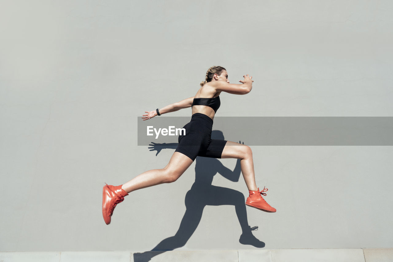 Young athlete jumping by gray wall on sunny day