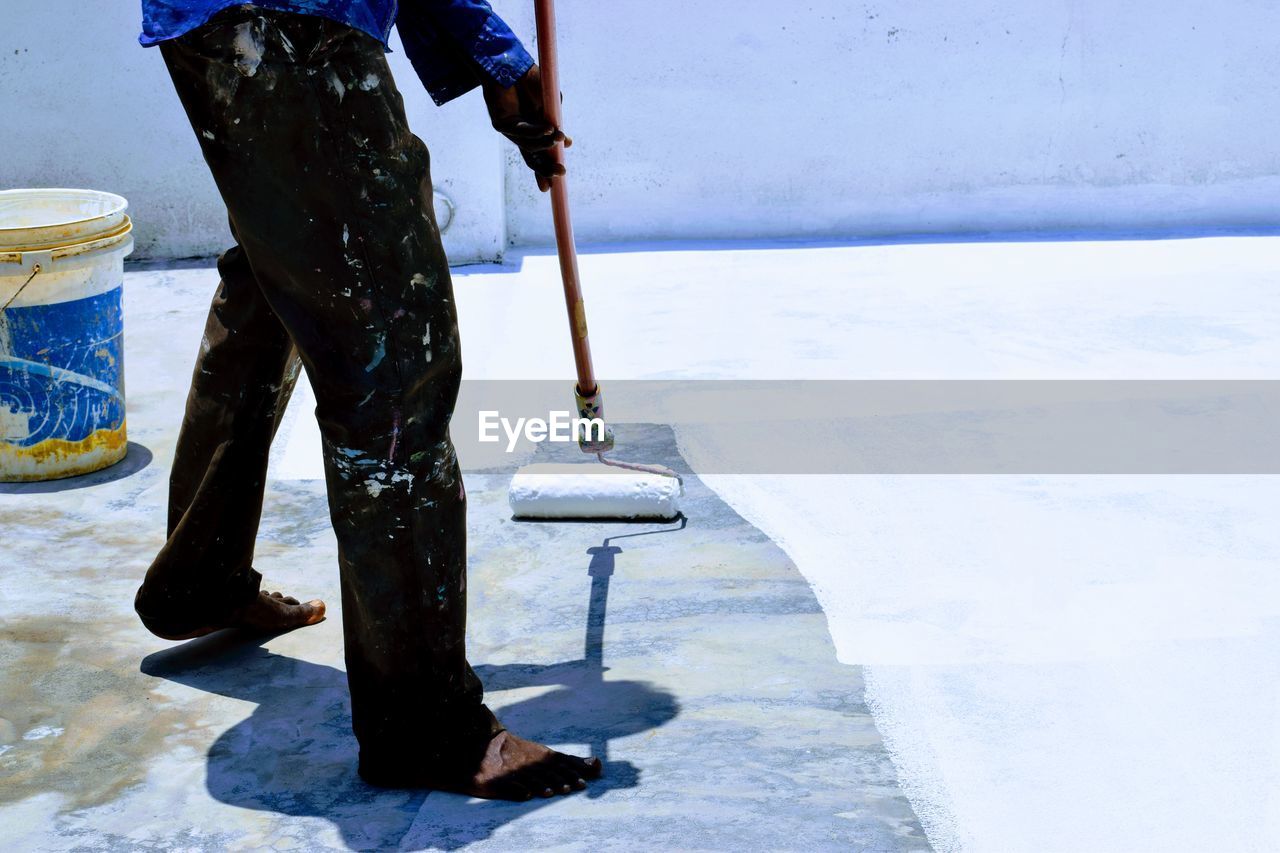 Low section of painter painting floor with paint roller