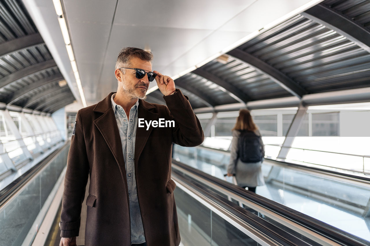 Man holding sunglasses while standing on escalator