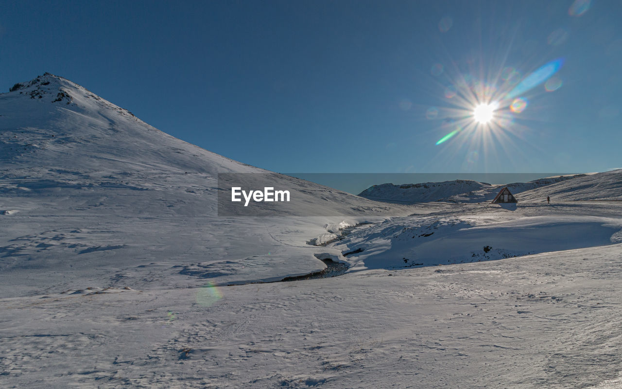 Panoramic view of chalet house in snow covered mountains with sun and camera flare on a clear day