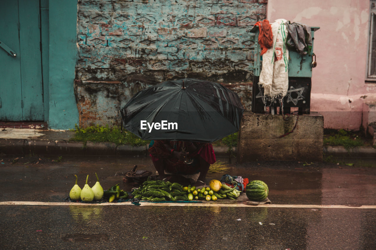 REAR VIEW OF WOMAN WITH UMBRELLA STANDING ON WET WALL