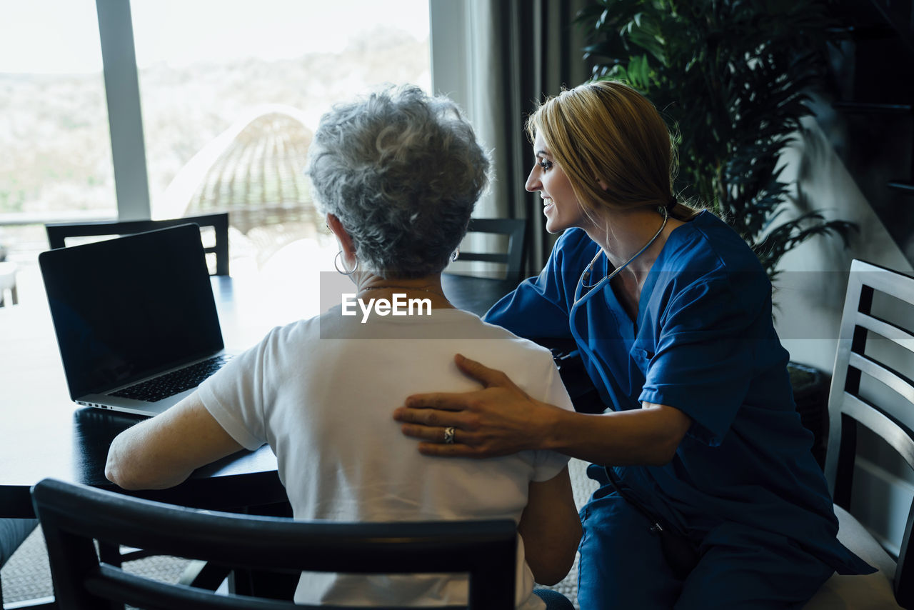 Home caregiver discussing over laptop computer with senior woman at dining table