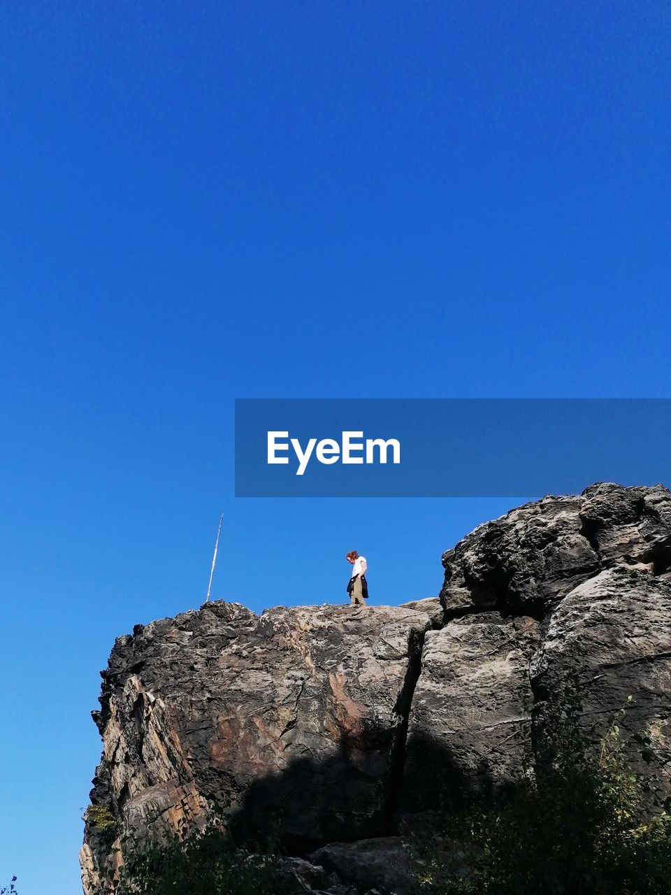 sky, blue, one person, clear sky, rock, nature, mountain, leisure activity, copy space, adventure, full length, activity, adult, cliff, day, low angle view, men, beauty in nature, lifestyles, scenics - nature, holiday, standing, vacation, terrain, trip, sports, sunny, outdoors, climbing, travel, sea, land, rock formation, hiking, extreme sports, rock climbing, sunlight, challenge, tranquility, non-urban scene, travel destinations, remote, exploration, young adult, mountain range, tranquil scene, determination