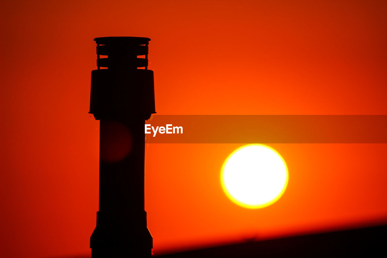 Low angle view of silhouette chimney against orange sky