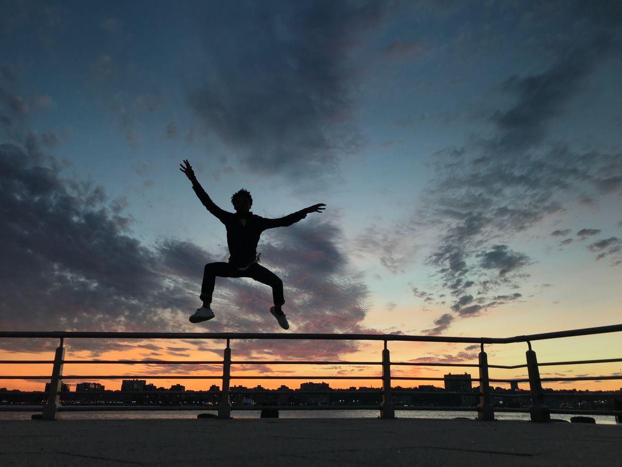 Silhouette man jumping against river during sunset