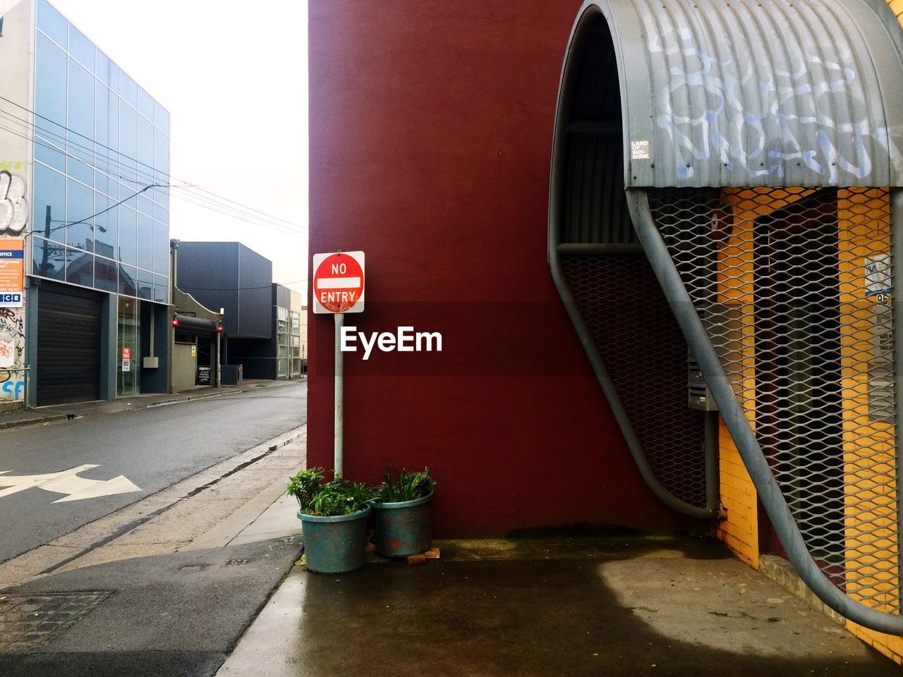 No entry sign amidst potted plants and wall by street