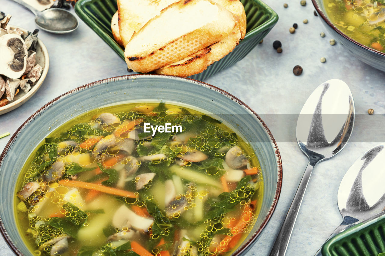 A bowl of soup with mushrooms and spinach leaves.