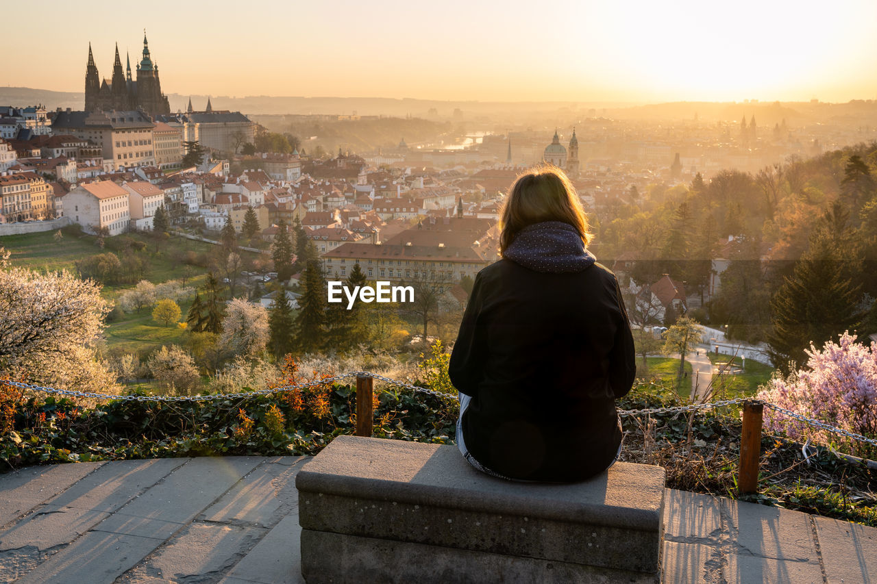 Rear view of woman relaxing outside in city park and enjoying view of prague, beautiful sunrise