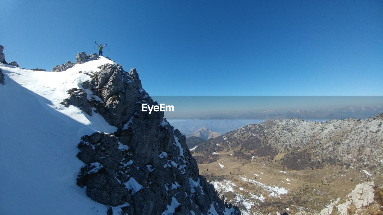 Distant view of woman standing on mountain against sky during winter