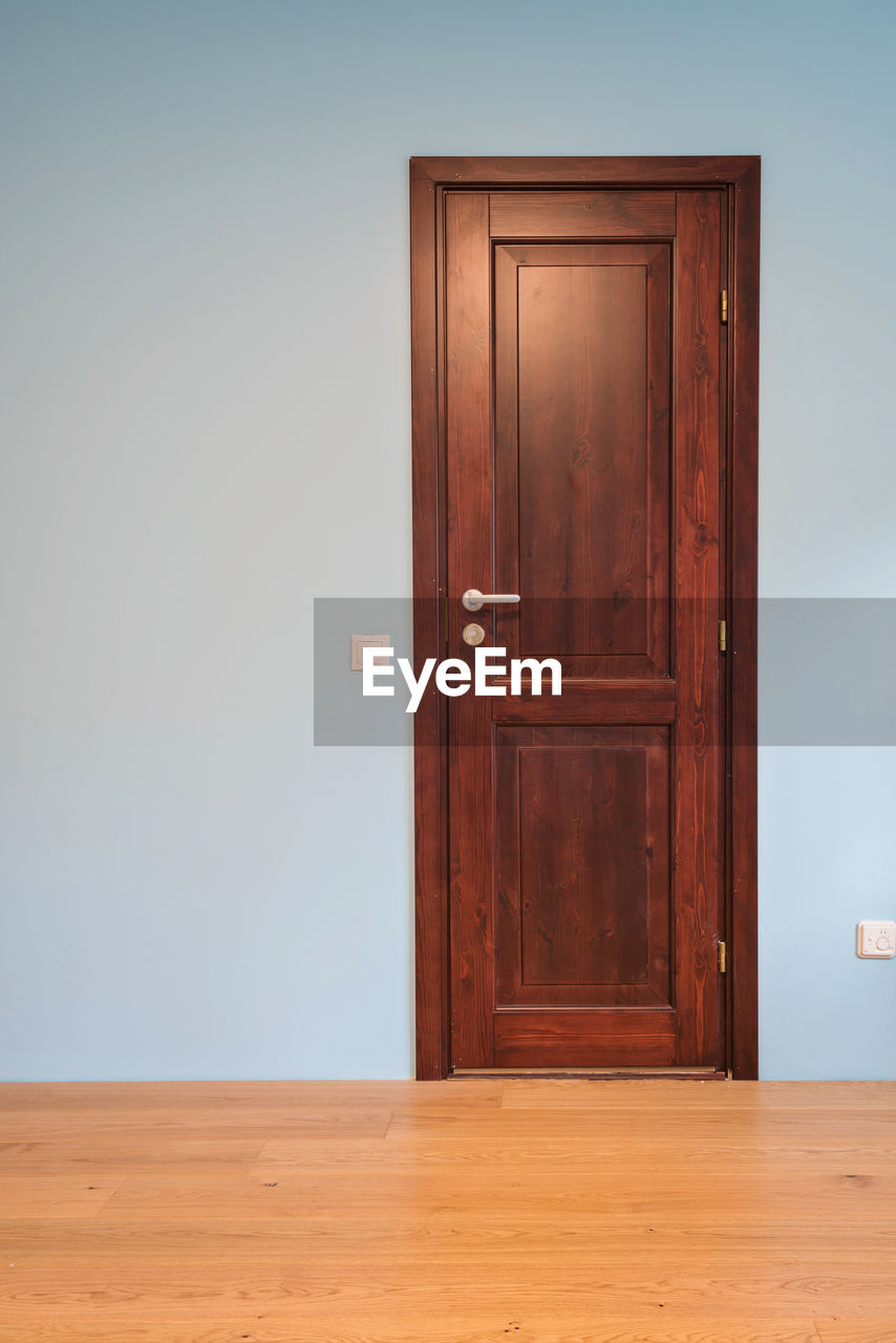 Frontal view to the wooden door in home interior room with wooden floors and blue walls.