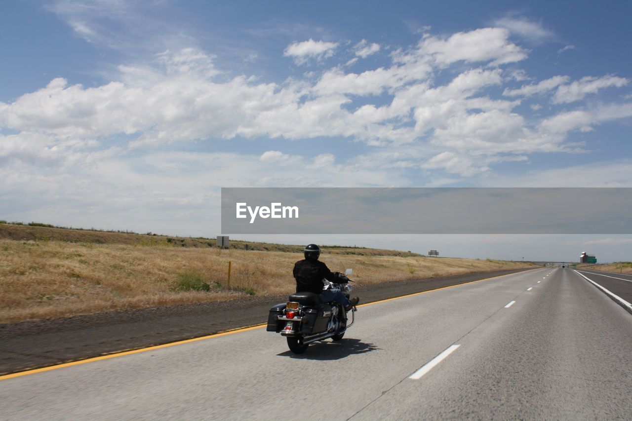 Man cycling on road against sky