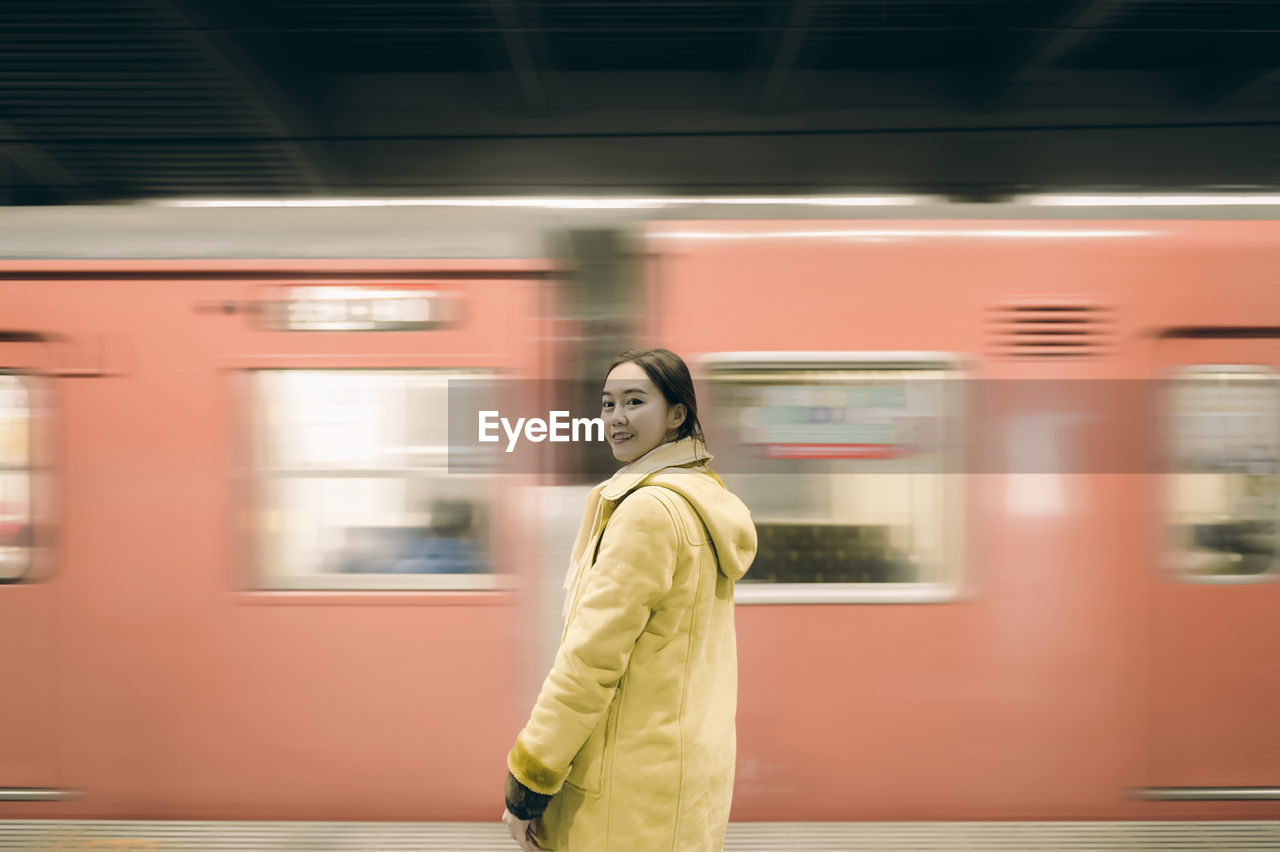 Portrait of woman standing against train moving at railroad station