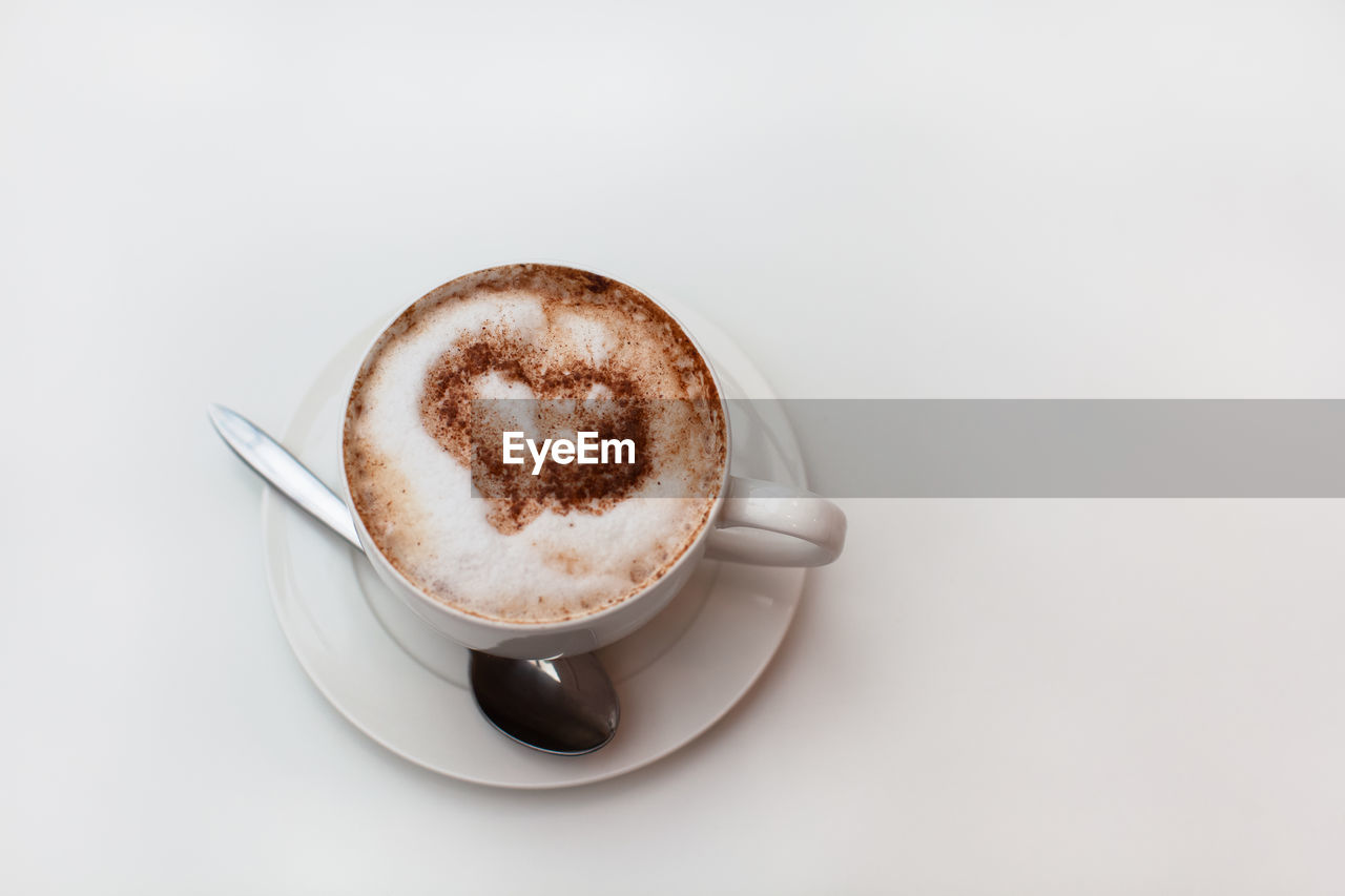 Cappuccino cup on white table background. foam is decorated with cinnamon heart. copy space. 