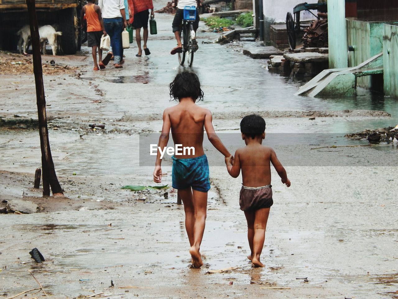 Rear view of boy and girl walking on wet footpath