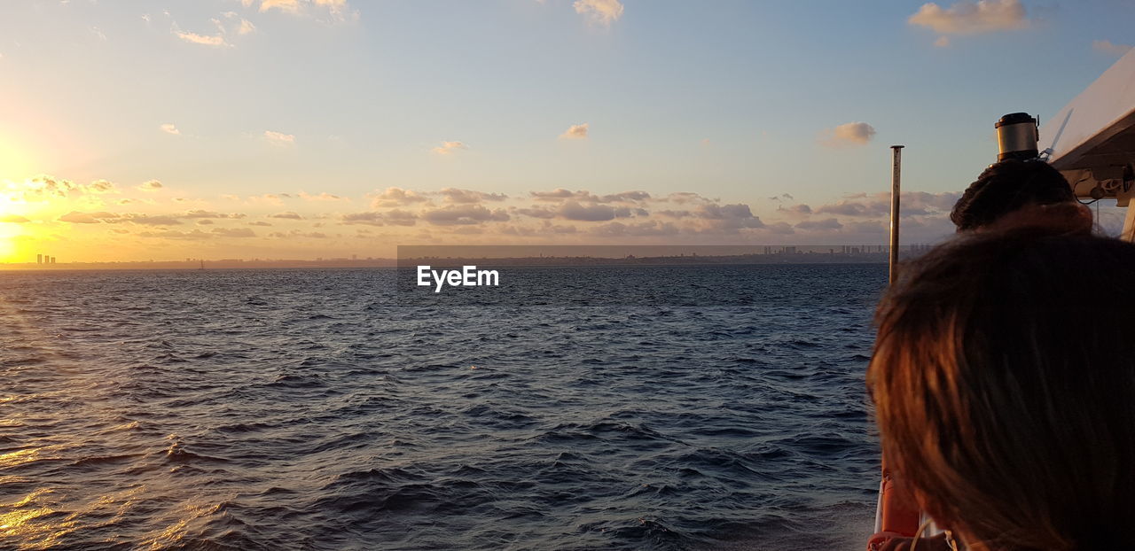 REAR VIEW OF WOMAN AT SEA AGAINST SKY