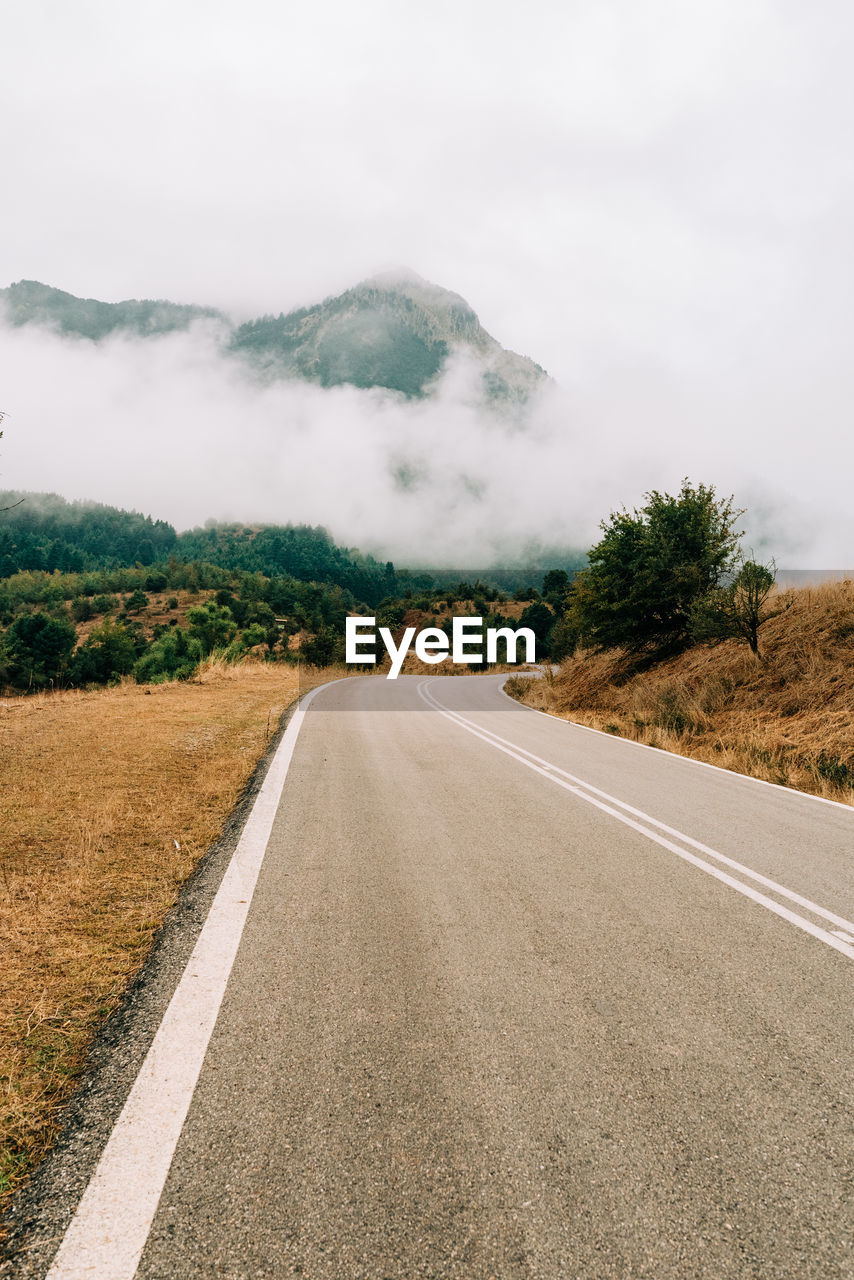 Empty road leading towards mountains against sky