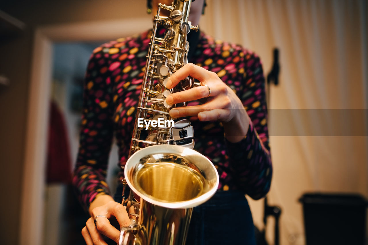 Midsection of woman playing saxophone while practicing at studio