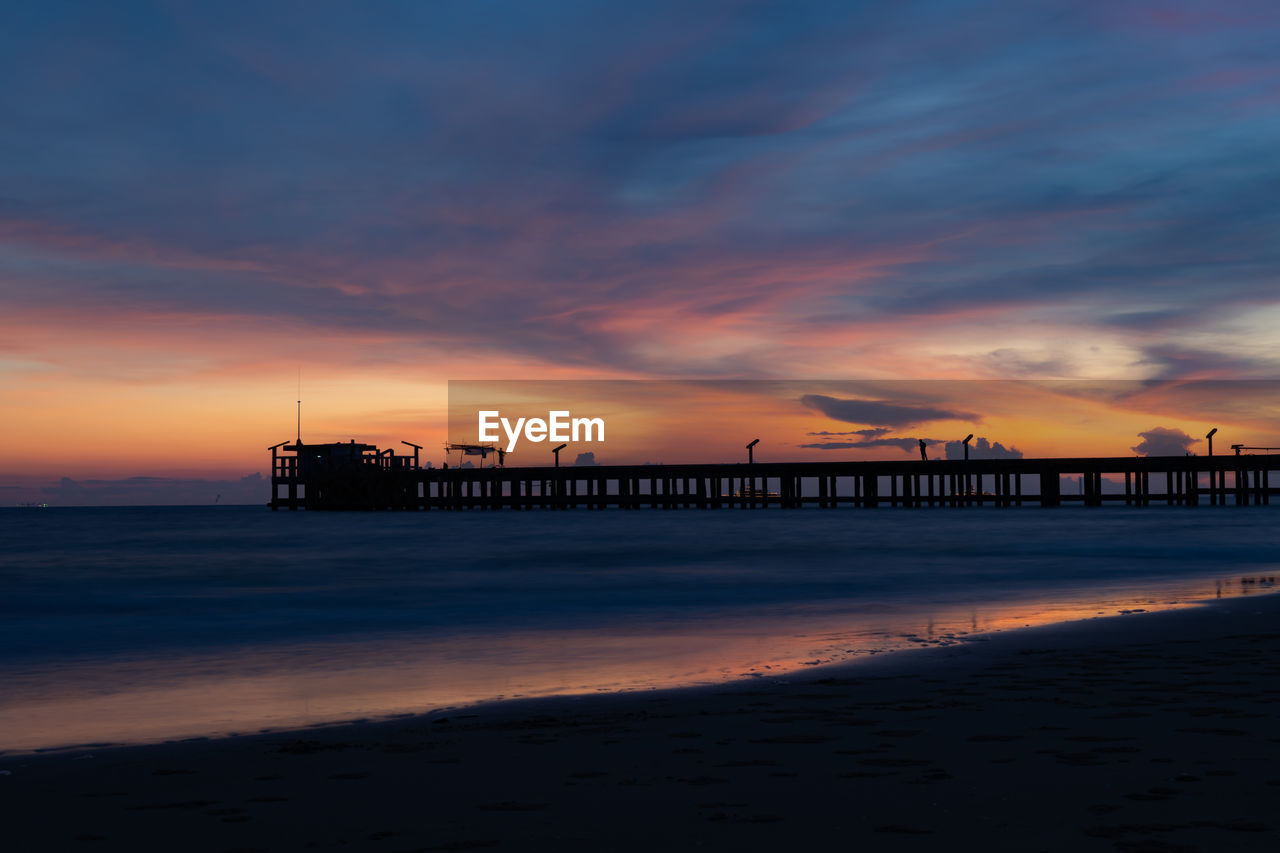 SILHOUETTE PIER ON BEACH AGAINST ORANGE SKY