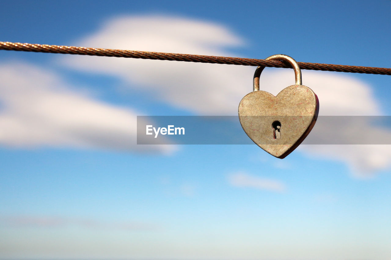 Close-up of heart shape padlock on cable against sky