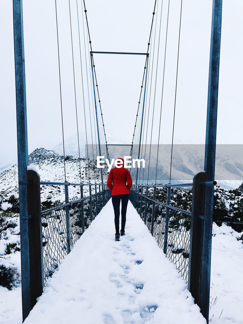 Rear view full length of woman walking on footbridge during winter