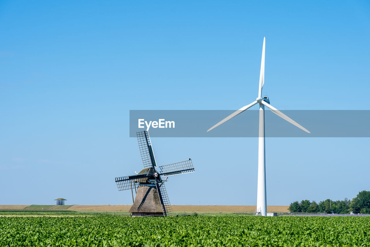 An old traditional windmill among a number of modern wind turbines under a clear blue sky
