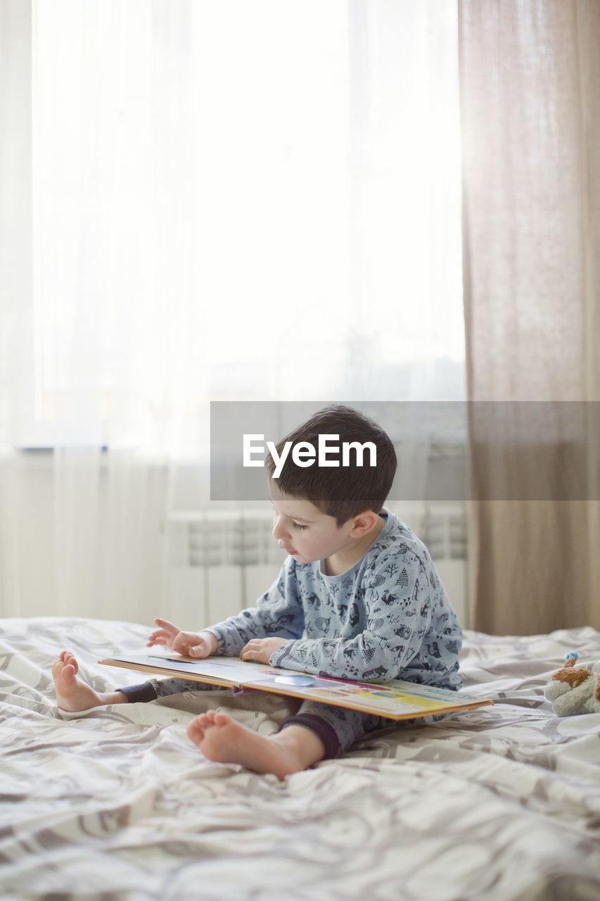 Boy reading book on bed