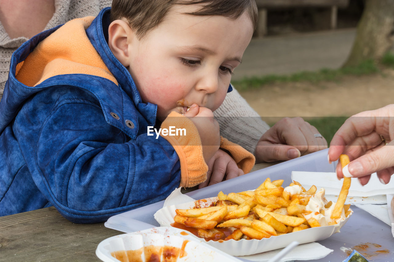 Close-up of boy eating french fries while sitting with mother at table