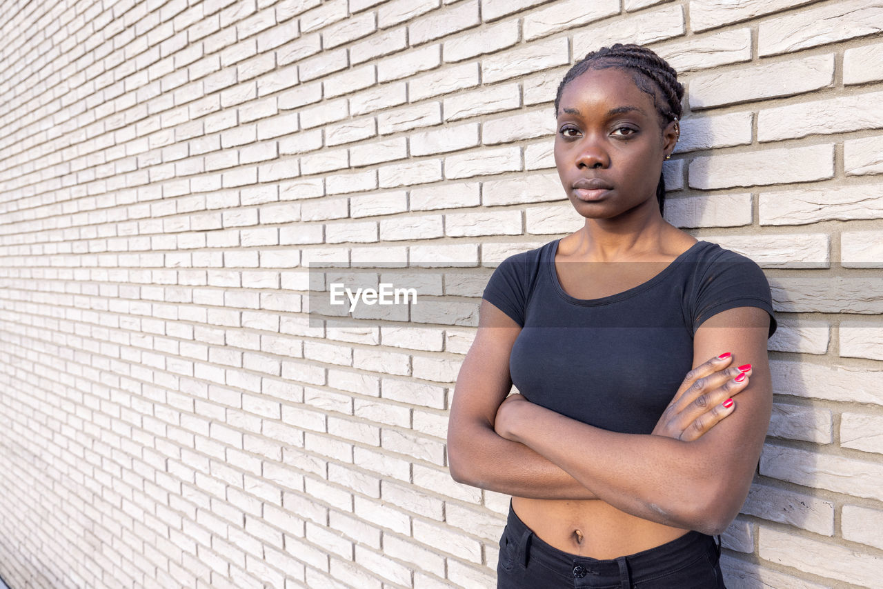 portrait of young woman standing against brick wall