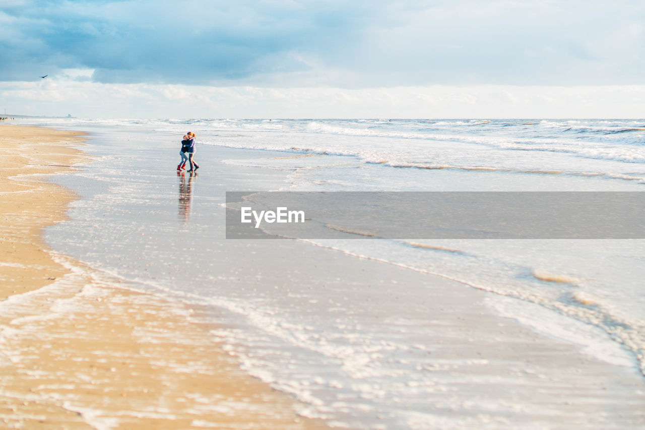 FULL LENGTH OF MAN STANDING AT BEACH AGAINST SKY