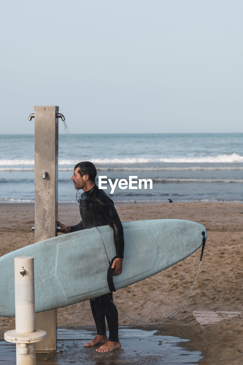 Full length of man with surfboard on beach against sky