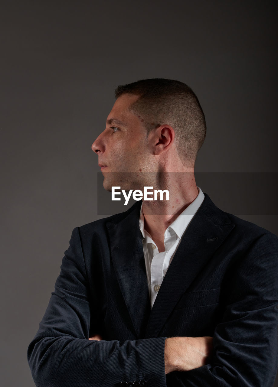 one person, adult, studio shot, men, indoors, business, formal wear, portrait, businessman, waist up, gray background, gray, looking, person, mature adult, looking away, serious, contemplation, emotion, clothing, arms crossed, tuxedo, black, shaved head, standing, facial expression