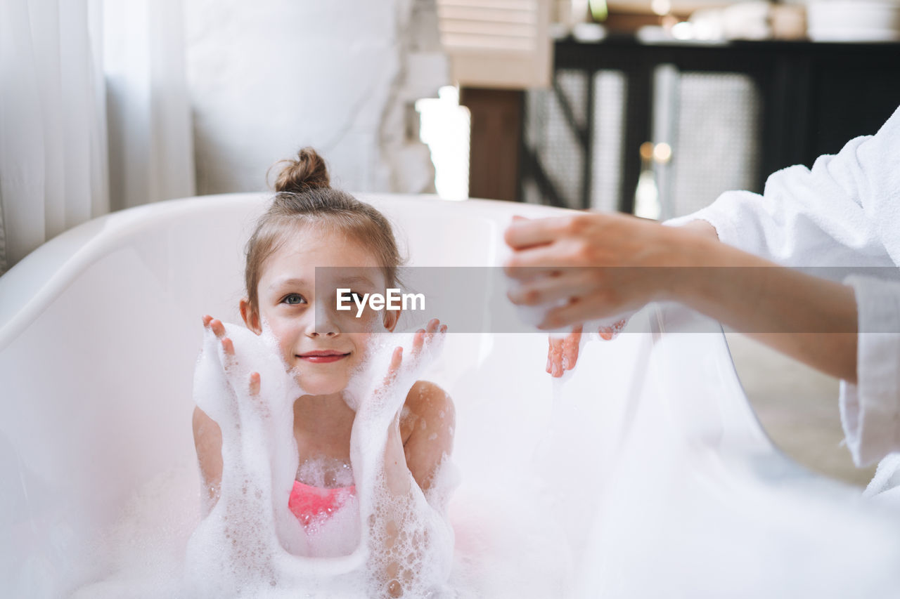 Young mother woman and little tween girl daughter having fun in the bath with foam at home