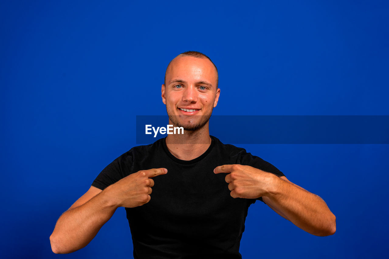 PORTRAIT OF SMILING MAN STANDING AGAINST GRAY BACKGROUND