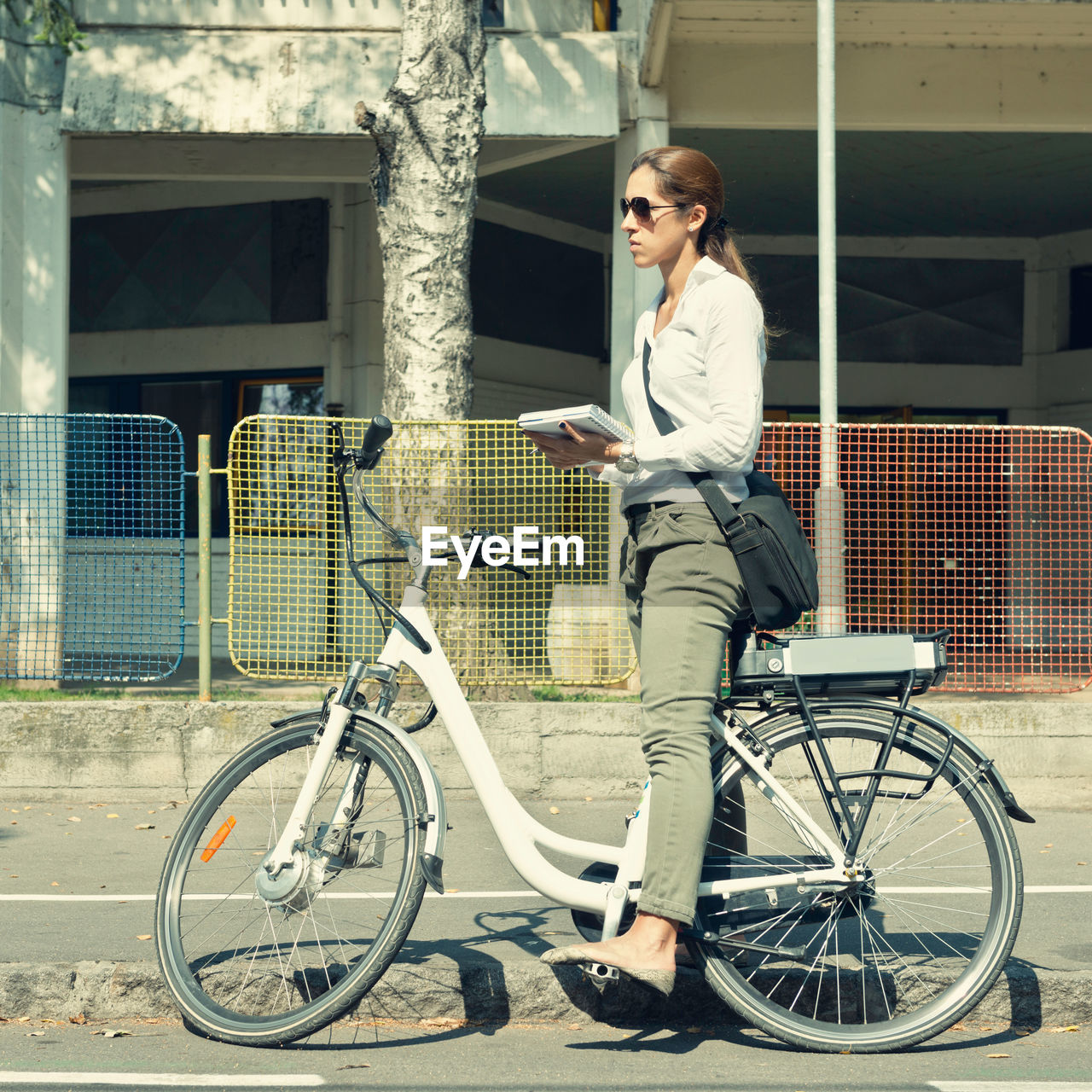Side view of woman holding diary with bicycle standing on road