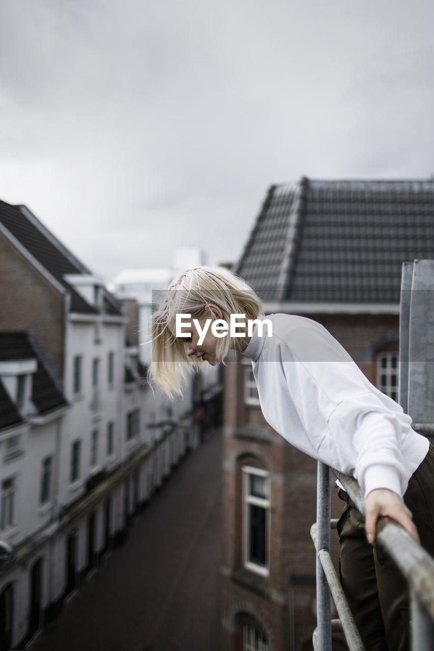 Side view of woman looking down while leaning on balcony railing