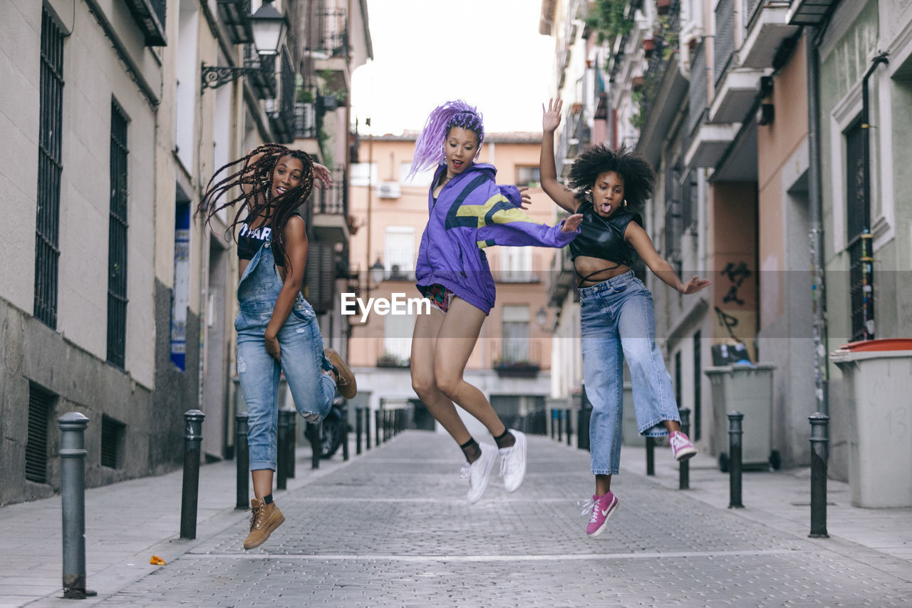 Full length of female friends jumping on street in city