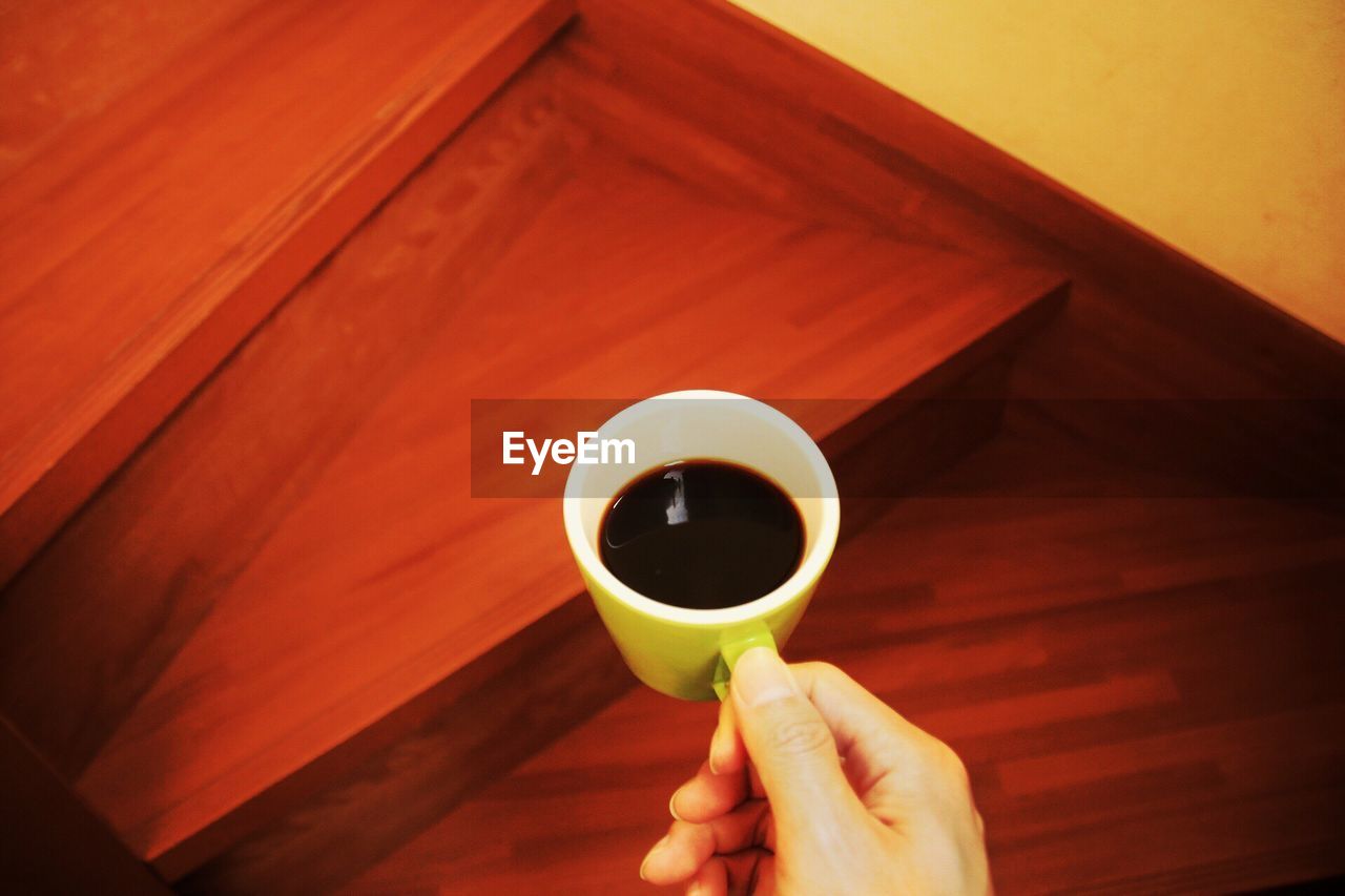 CLOSE-UP OF HAND HOLDING COFFEE CUP WITH SPOON