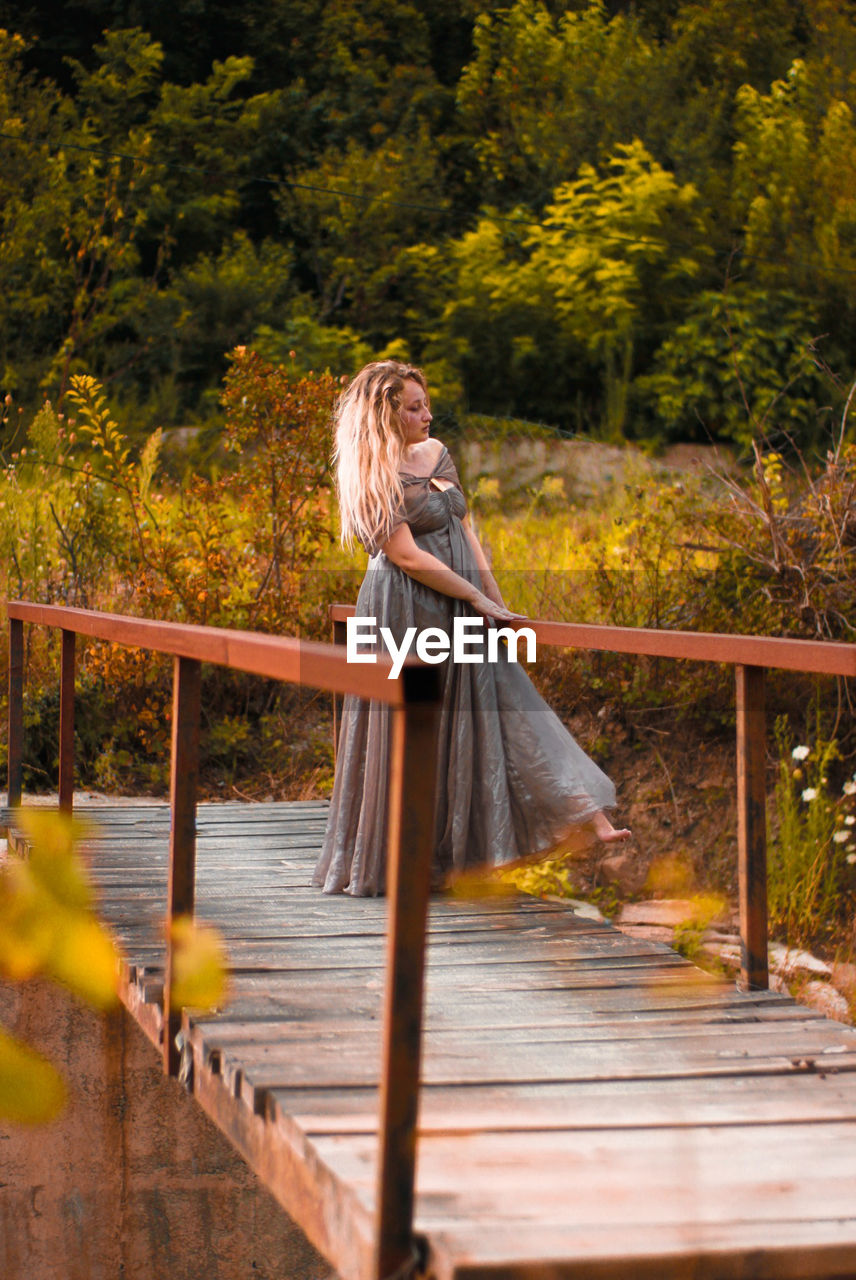 Woman wearing evening gown while standing footbridge against plants