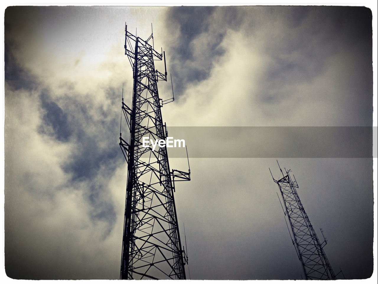 Low angle view of electricity pylons against cloudy sky