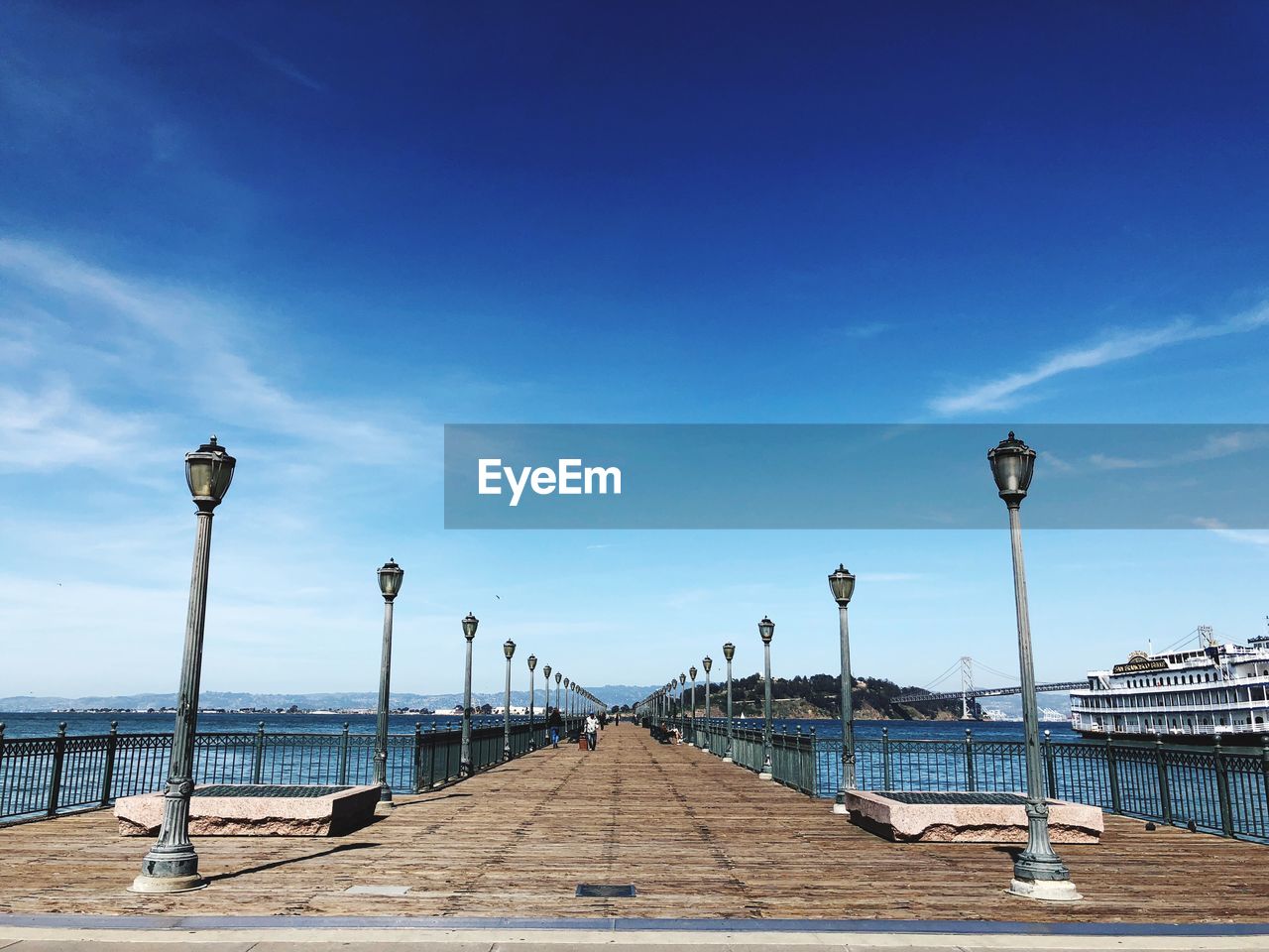 Street lights on footpath by sea against blue sky